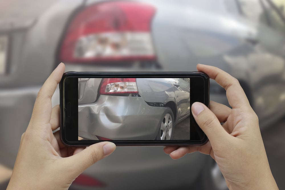 Close-up of someone taking a picture of a car accident damage with their phone