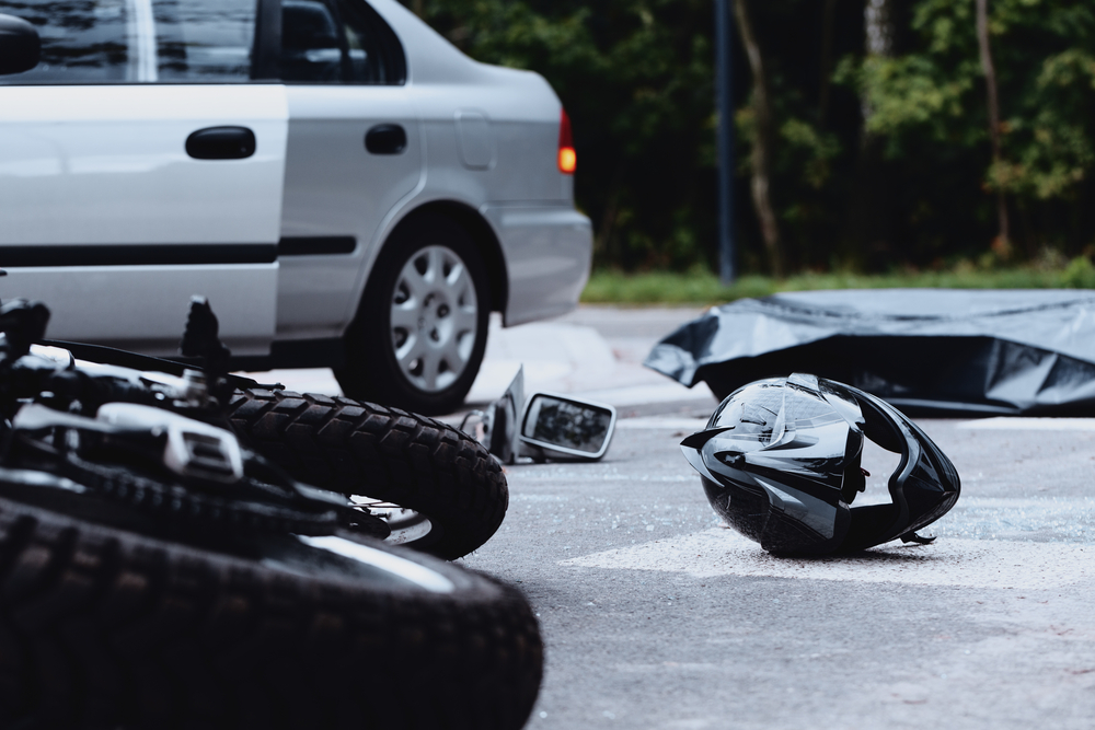 Motorcycle and helmet on street after crash, car in background