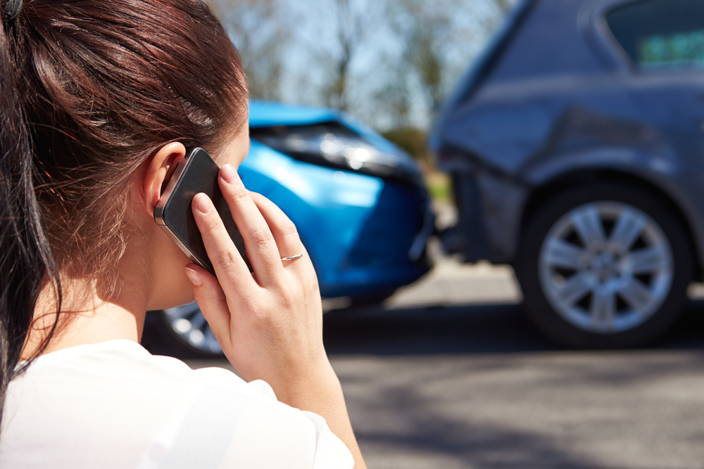 Close-up of young woman friend behind, talking on phone, car crash in background