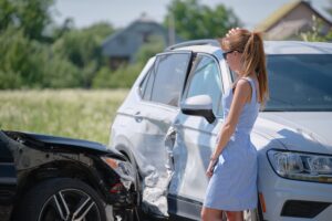 Young female driver standing by car after accident