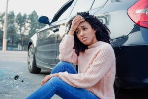 Distressed young woman beside car crash