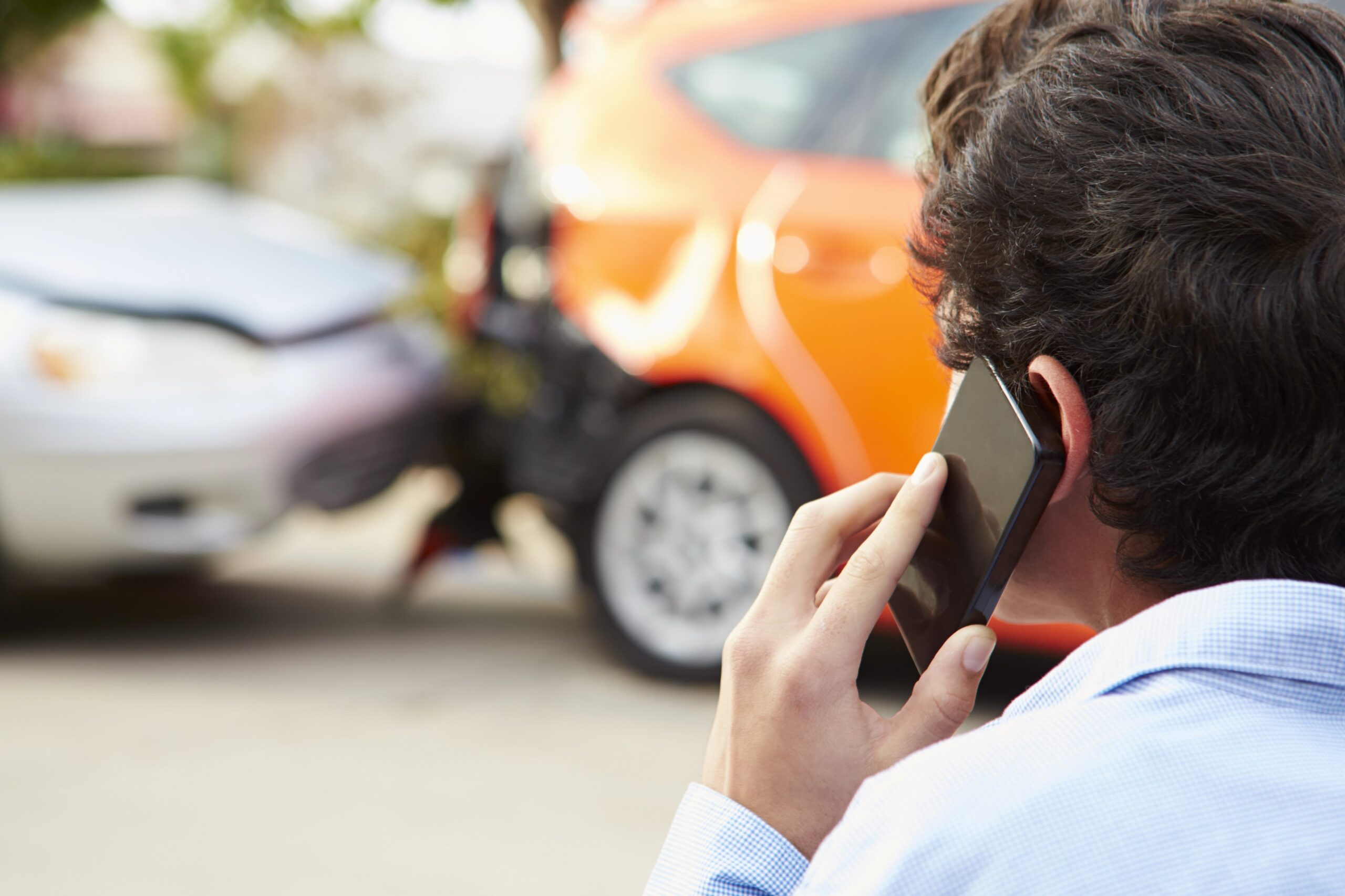 Close-up of man on phone looking at car crash