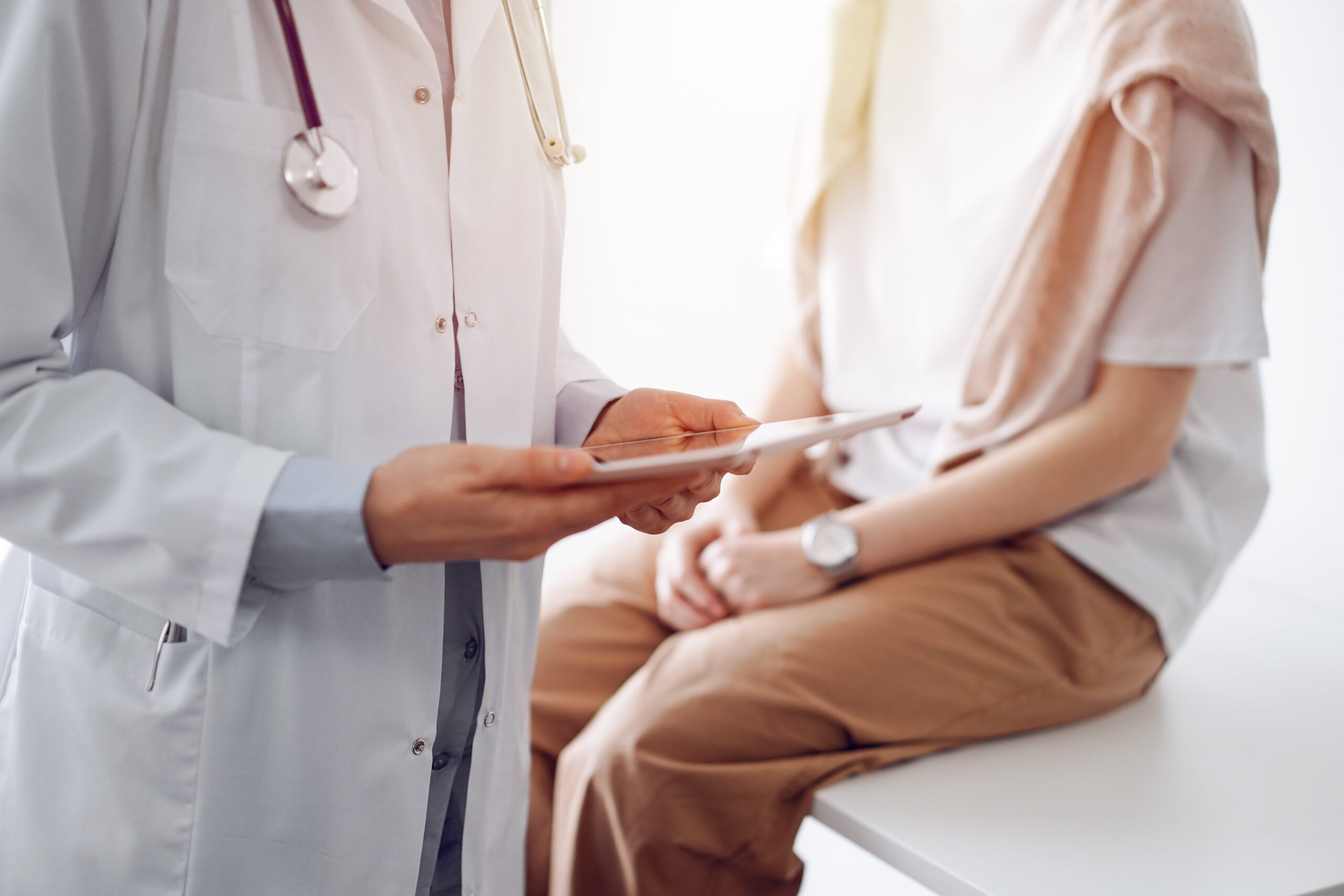 Cropped photo of doctor standing beside patient sitting on table